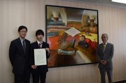 作品名「コメディから二歩横へ」 感謝状を手にする齊藤さん。 学長(左)、吉岡教授(右)とともに記念撮影 (於、学長執務室)
